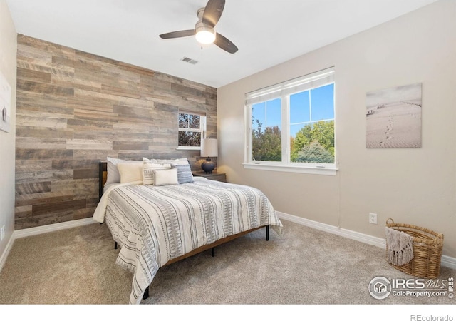 carpeted bedroom featuring ceiling fan and wooden walls