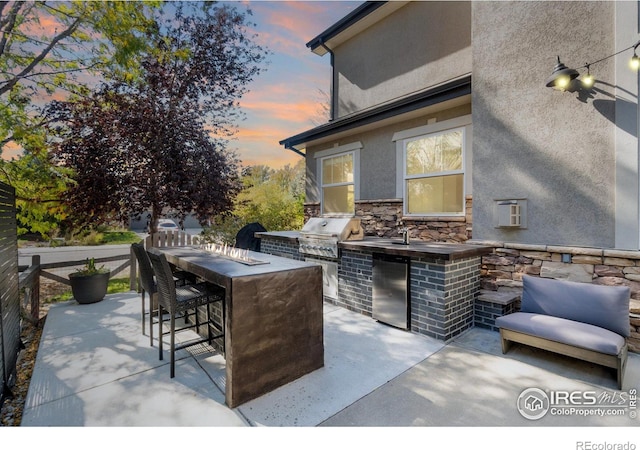 patio terrace at dusk with an outdoor kitchen, exterior bar, and area for grilling