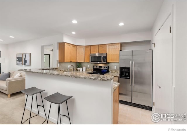 kitchen with appliances with stainless steel finishes, sink, backsplash, light stone counters, and kitchen peninsula