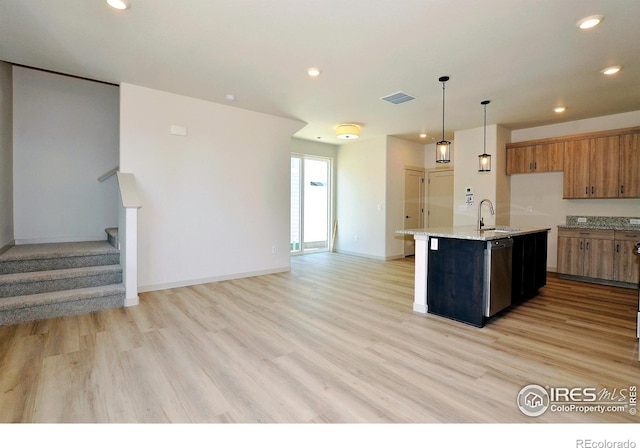 kitchen featuring light wood-type flooring, stainless steel dishwasher, a kitchen island with sink, sink, and decorative light fixtures