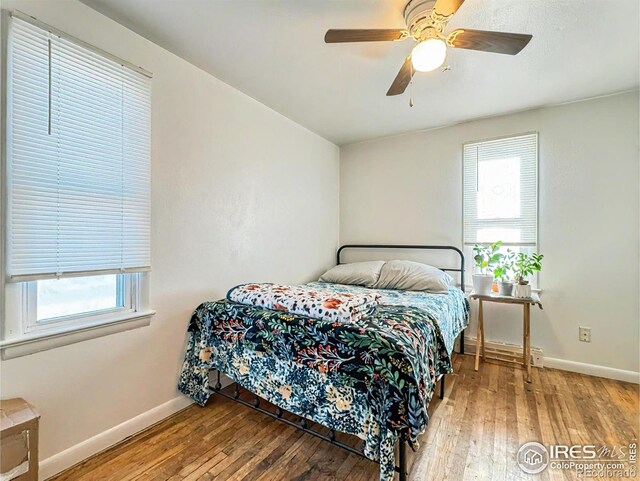 bedroom with baseboard heating, multiple windows, ceiling fan, and hardwood / wood-style flooring