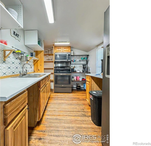 kitchen with sink, vaulted ceiling, decorative backsplash, light wood-type flooring, and stainless steel appliances