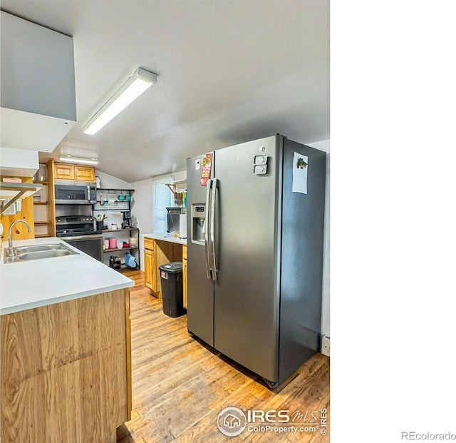 kitchen featuring appliances with stainless steel finishes, vaulted ceiling, light hardwood / wood-style flooring, and sink