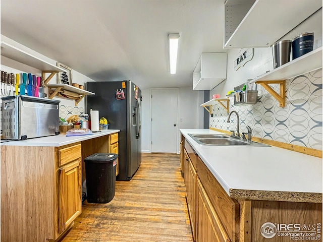 kitchen with light wood-type flooring, sink, stainless steel refrigerator with ice dispenser, and tasteful backsplash