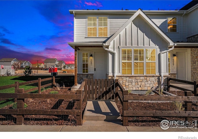 view of front of home with stone siding, fence, and board and batten siding