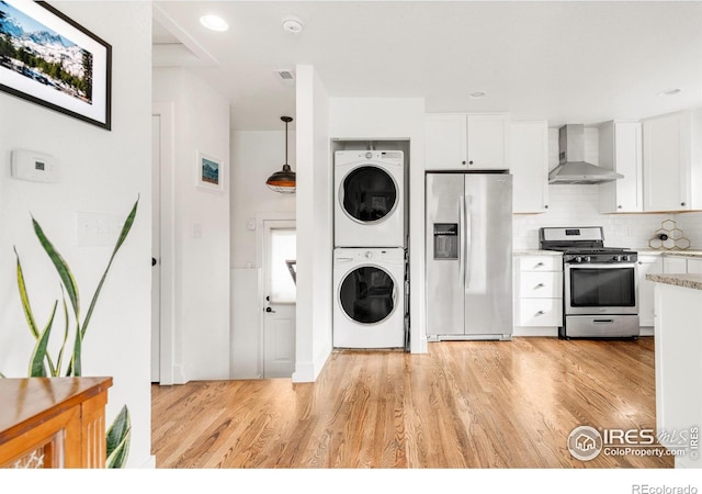 kitchen with white cabinetry, wall chimney range hood, stainless steel appliances, and stacked washing maching and dryer