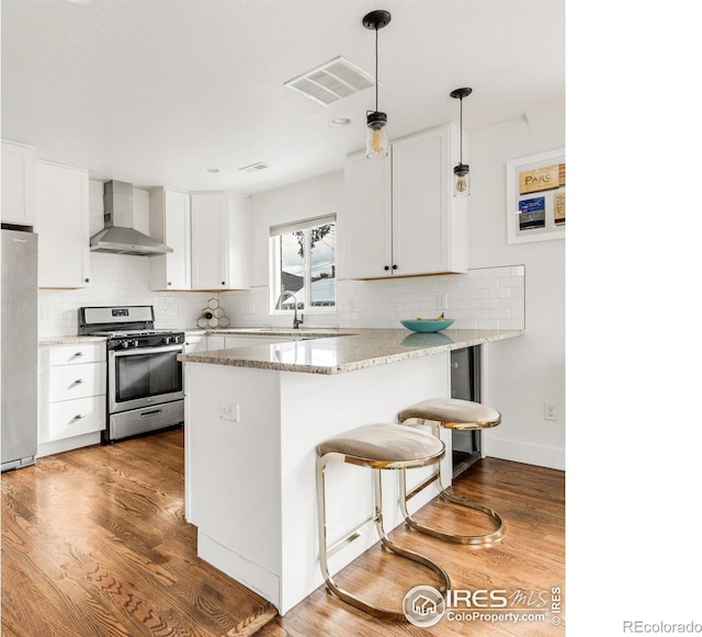 kitchen with a breakfast bar, white cabinets, wall chimney range hood, kitchen peninsula, and stainless steel appliances