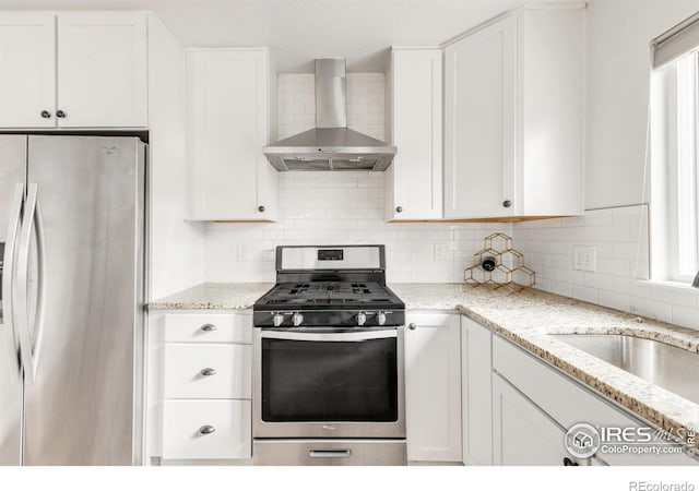 kitchen featuring white cabinetry, light stone counters, wall chimney range hood, and appliances with stainless steel finishes