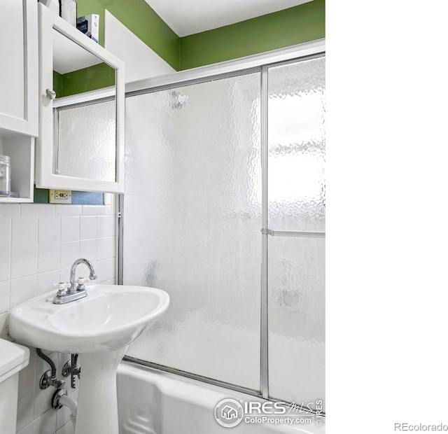 bathroom with decorative backsplash, toilet, tile walls, and bath / shower combo with glass door