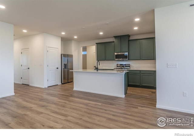 kitchen with sink, stainless steel appliances, a kitchen island with sink, and light hardwood / wood-style flooring