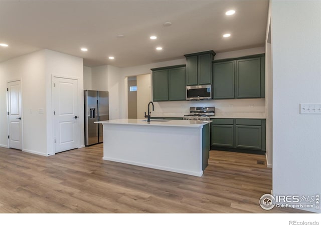 kitchen with a center island with sink, green cabinets, sink, wood-type flooring, and stainless steel appliances