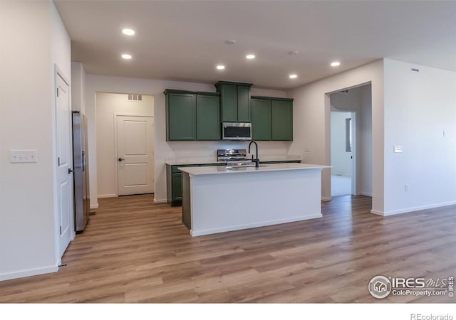 kitchen featuring light wood-type flooring, stainless steel appliances, sink, a center island with sink, and green cabinets