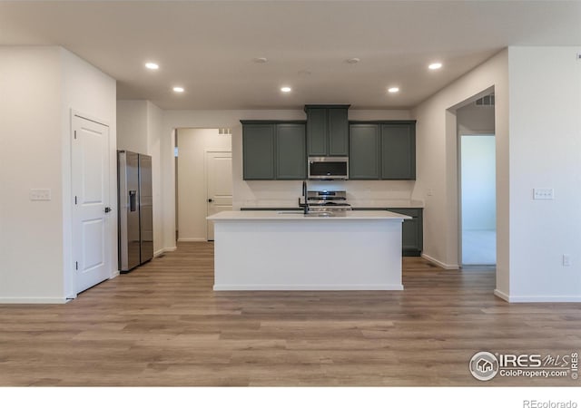 kitchen with sink, a center island with sink, light wood-type flooring, and appliances with stainless steel finishes