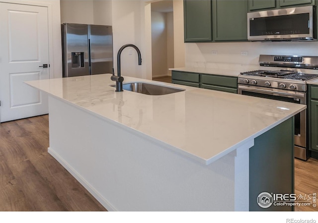 kitchen featuring a kitchen island with sink, sink, green cabinetry, light stone counters, and stainless steel appliances