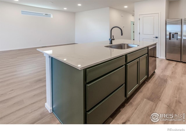 kitchen with sink, stainless steel appliances, light stone counters, light hardwood / wood-style flooring, and a center island with sink