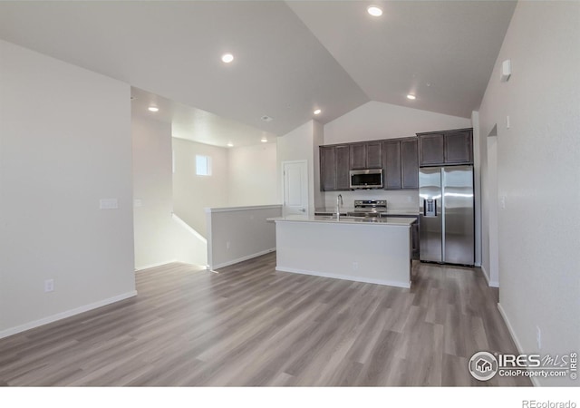 kitchen with a kitchen island with sink, sink, light wood-type flooring, appliances with stainless steel finishes, and dark brown cabinetry