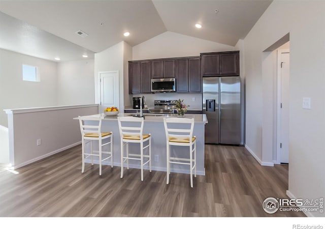 kitchen with dark hardwood / wood-style flooring, dark brown cabinets, an island with sink, and appliances with stainless steel finishes