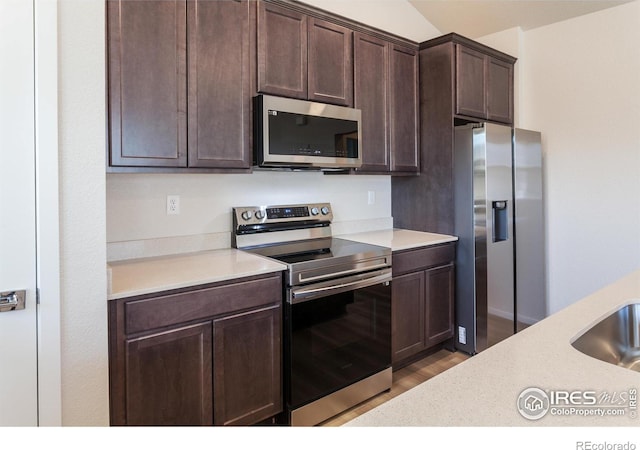 kitchen featuring hardwood / wood-style floors, dark brown cabinets, stainless steel appliances, and vaulted ceiling