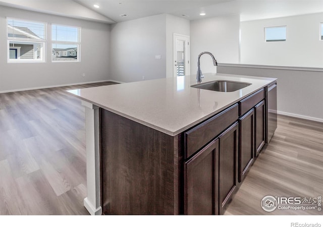 kitchen featuring a kitchen island with sink, sink, vaulted ceiling, stainless steel dishwasher, and light hardwood / wood-style flooring