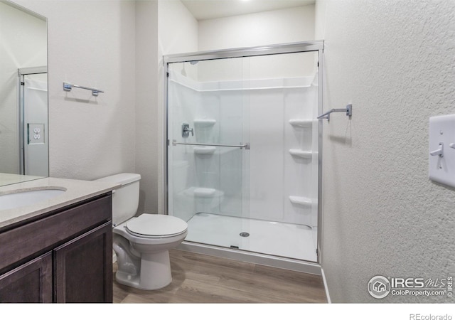 bathroom featuring a shower with door, vanity, wood-type flooring, and toilet