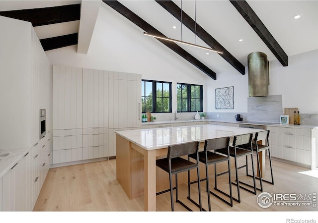 kitchen featuring a large island, wall chimney exhaust hood, light hardwood / wood-style floors, a breakfast bar area, and white cabinets