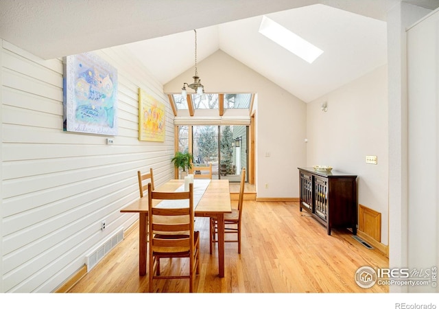 dining area with lofted ceiling with skylight, an inviting chandelier, and light hardwood / wood-style flooring