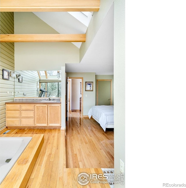 bedroom with a skylight, high vaulted ceiling, light hardwood / wood-style floors, beamed ceiling, and wood walls