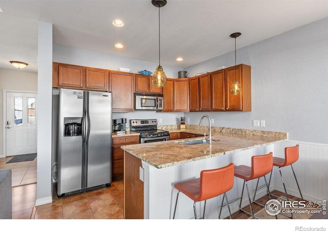 kitchen with a peninsula, appliances with stainless steel finishes, a sink, and brown cabinets