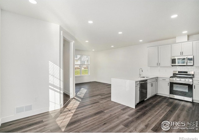 kitchen featuring appliances with stainless steel finishes, tasteful backsplash, white cabinetry, sink, and dark wood-type flooring