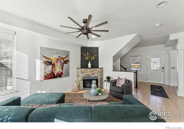 living room featuring a stone fireplace, ceiling fan, and light hardwood / wood-style flooring