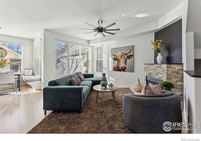 living room with wood-type flooring, a stone fireplace, and ceiling fan