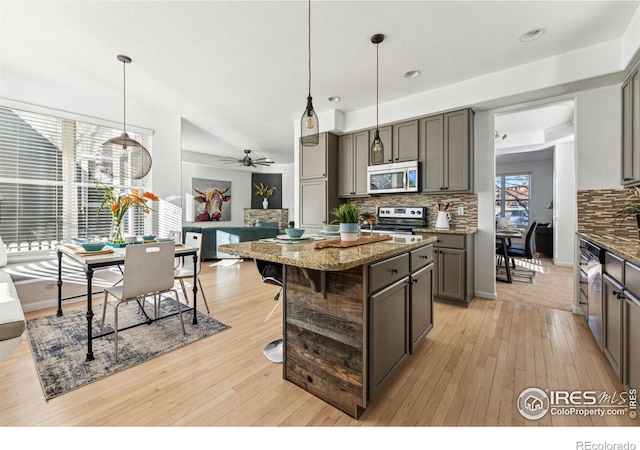 kitchen featuring a center island, ceiling fan, appliances with stainless steel finishes, decorative light fixtures, and light stone counters