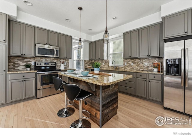 kitchen with decorative backsplash, appliances with stainless steel finishes, light stone counters, gray cabinetry, and a center island