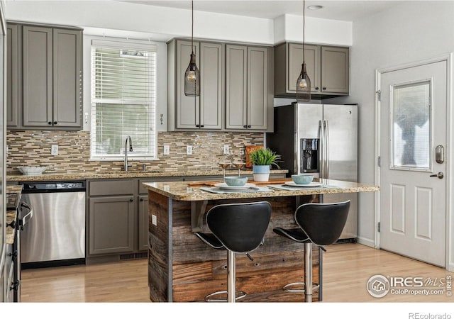 kitchen featuring gray cabinetry, a center island, sink, light stone countertops, and stainless steel appliances