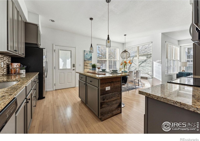 kitchen featuring pendant lighting, dishwasher, tasteful backsplash, a kitchen island, and light stone counters