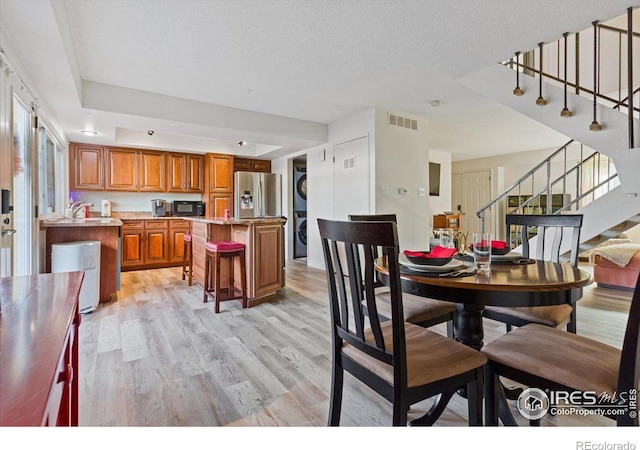 dining area with stacked washer / drying machine, light hardwood / wood-style floors, and a textured ceiling