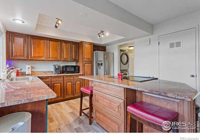 kitchen with stacked washer and clothes dryer, black appliances, a raised ceiling, sink, and light stone countertops