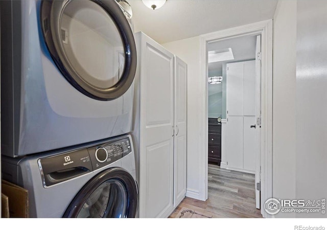 clothes washing area with stacked washer and clothes dryer and light wood-type flooring