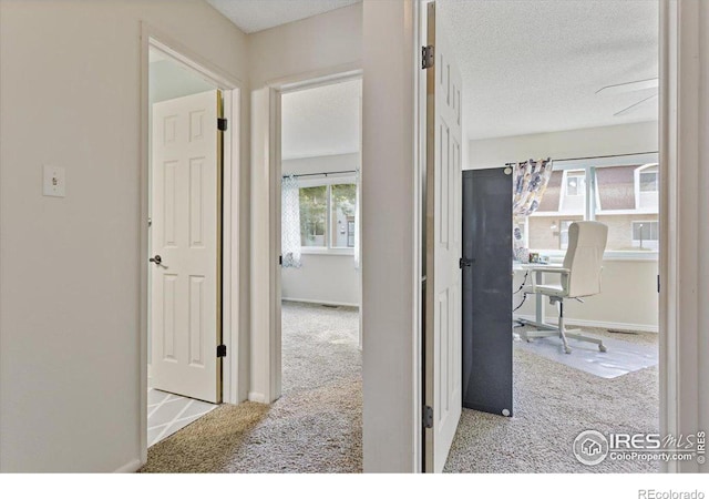 corridor featuring a textured ceiling and light colored carpet