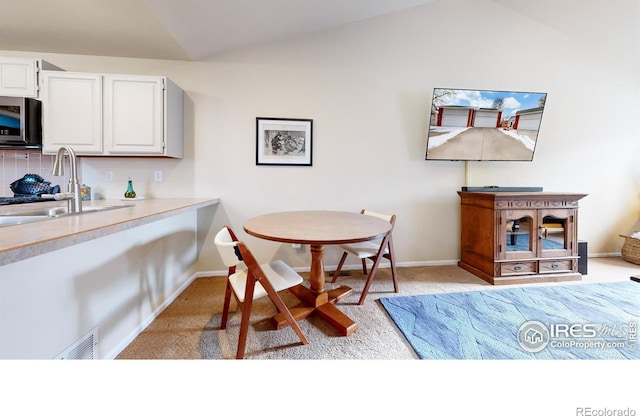 dining room featuring lofted ceiling, sink, and light carpet