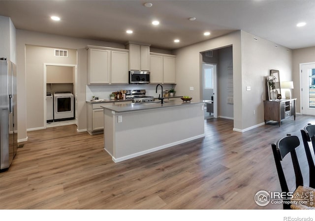 kitchen with white cabinetry, light hardwood / wood-style floors, a center island with sink, appliances with stainless steel finishes, and washing machine and dryer