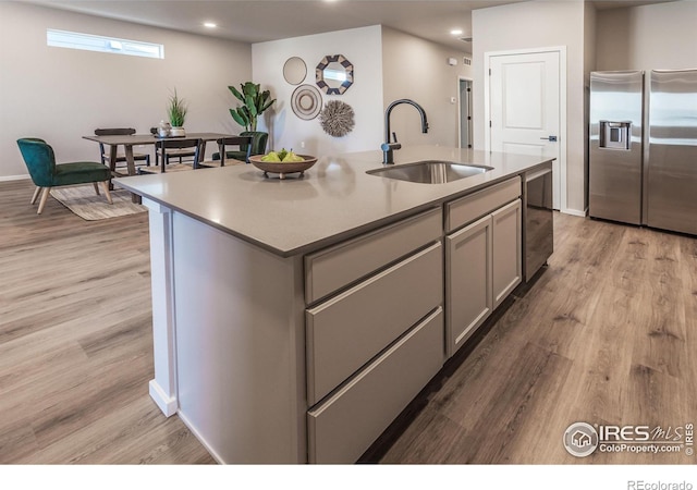 kitchen featuring gray cabinets, light hardwood / wood-style floors, a center island with sink, sink, and stainless steel appliances