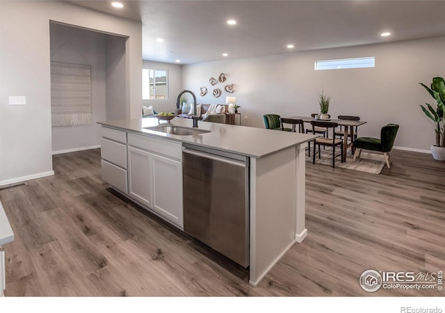 kitchen featuring white cabinetry, sink, hardwood / wood-style flooring, stainless steel dishwasher, and a center island with sink