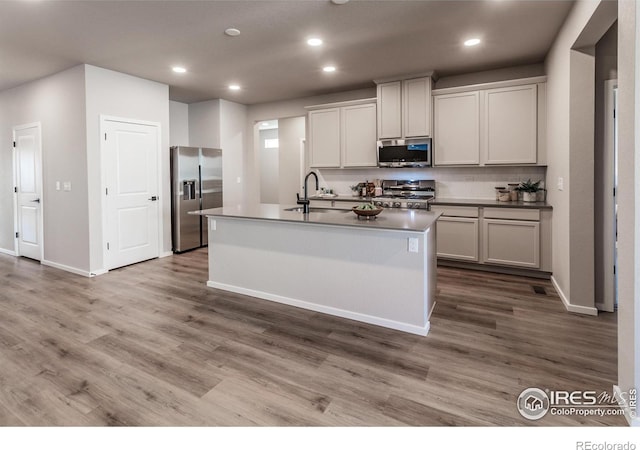 kitchen featuring decorative backsplash, wood-type flooring, sink, an island with sink, and stainless steel appliances