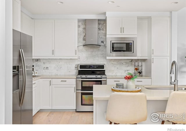 kitchen featuring a kitchen breakfast bar, white cabinetry, wall chimney range hood, and stainless steel appliances