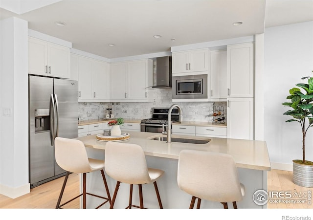 kitchen featuring sink, wall chimney exhaust hood, stainless steel appliances, a kitchen breakfast bar, and white cabinets