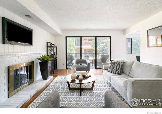 living room featuring hardwood / wood-style floors, a textured ceiling, and a brick fireplace