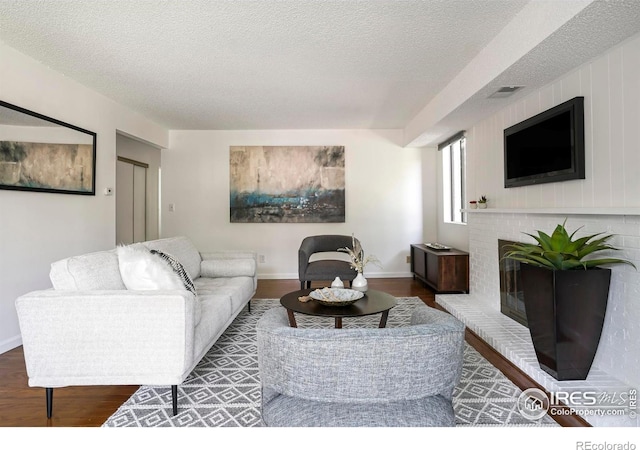 living room featuring hardwood / wood-style flooring, a textured ceiling, and a brick fireplace