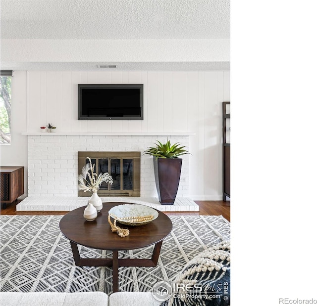 living room with dark hardwood / wood-style flooring, a textured ceiling, and a brick fireplace