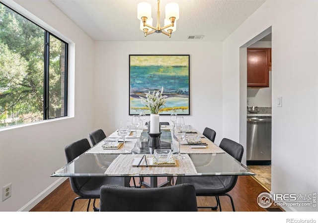 dining area with wood-type flooring, a textured ceiling, and an inviting chandelier